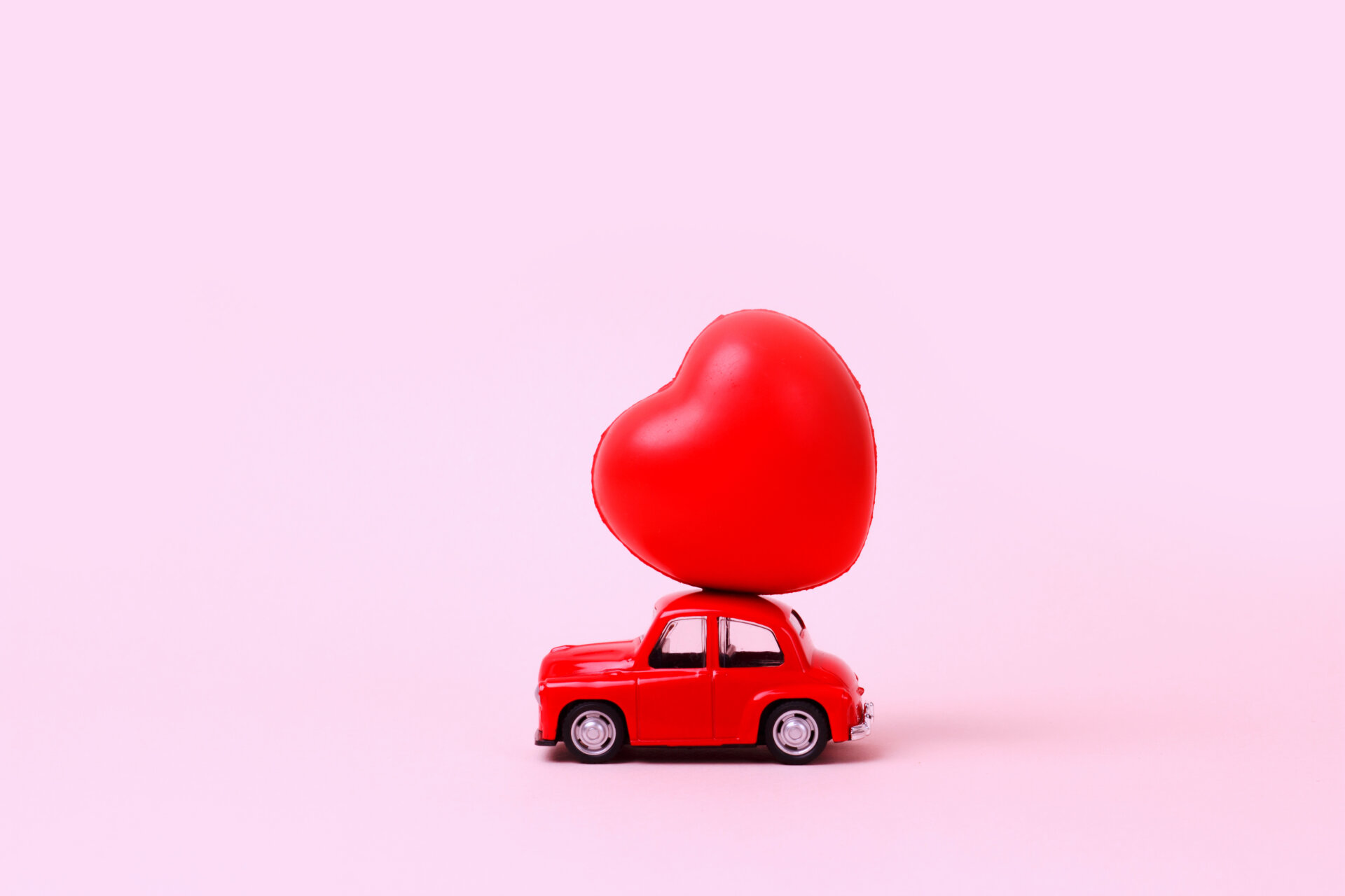 Small red retro toy car with heart on the roof. New Year, Christmas, Valentines Day, World Womans Day.